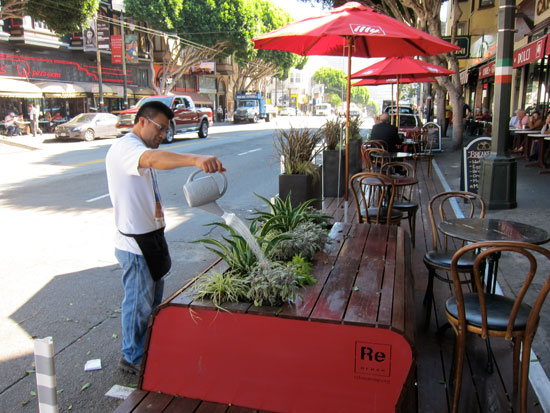 An employee of Cafe Greco waters the plants on the new parklet. All maintenance of the parklet is the responsibility of the property owner.