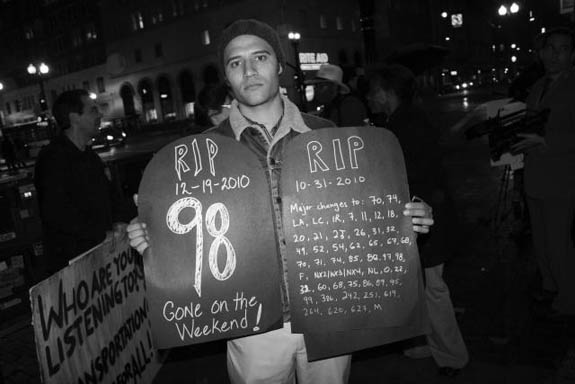 Colin Miller of Urban Habitat holds up gravestones in memory of bus lines that have been cut. Photo: Reginald James