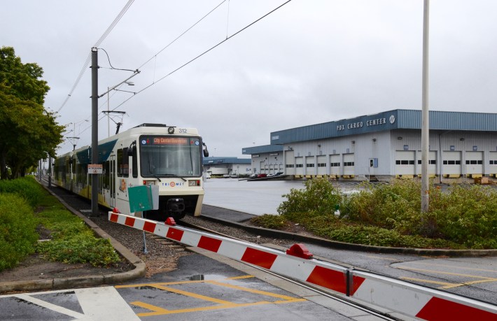 A Portland MAX train crossing an intersection. Railroad crossing gates could give the M-Ocean View all the speed advantages of a subway tunnel without any of the costs. Image: Wikiemedia commons.