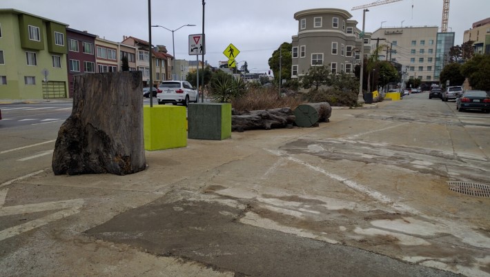 Although construction is not yet complete, the small park is really taking shape. Note the use of logs and concrete art to make sure cars can't intrude on this public space. Although it is permeable to pedestrians and slow moving bikes. Photo: Streetsblog.