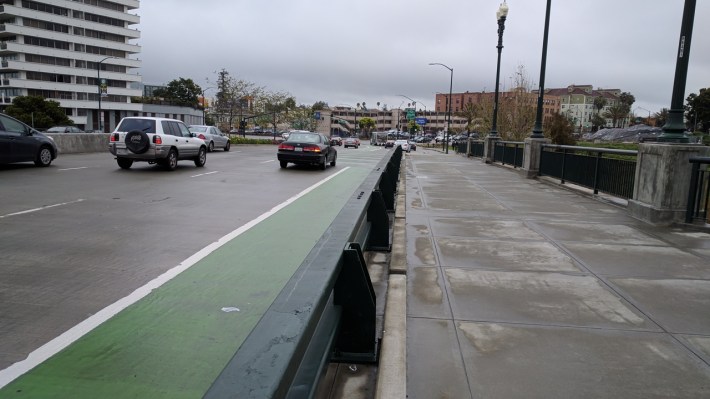 Why would traffic engineers go to all the trouble of putting in this barrier, but on the wrong side of the bike lane? Photo: Streetsblog/Rudick