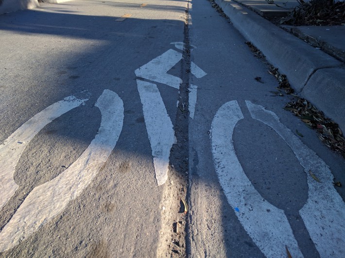 The wheel-grabbing groove through most of the center of the bike lane is just one of the hazards introduced by the lack of basic maintenance of the bike path.