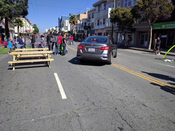 A car from a local resident had to wait behind pedestrians, in a temporary world where cars are subordinate.