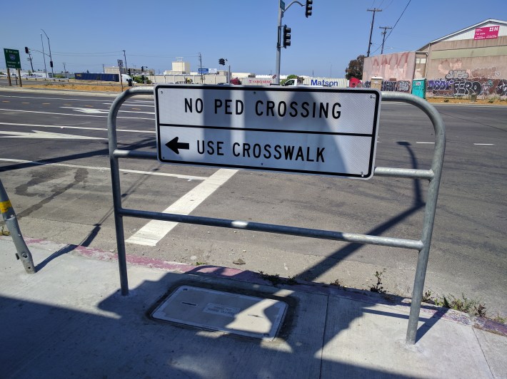 This Caltrans sign on 23rd Avenue in Oakland points to an imaginary crosswalk...and if you did get across, there's no sidewalk on the other side anyway. The same thinking that gave us this garbage is behind the OAAP designs. Photos: Streetsblog/Rudick