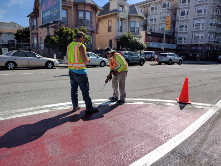 Workers filling holes with resin to glue down in the threaded piece of pipe that will hold the bollard