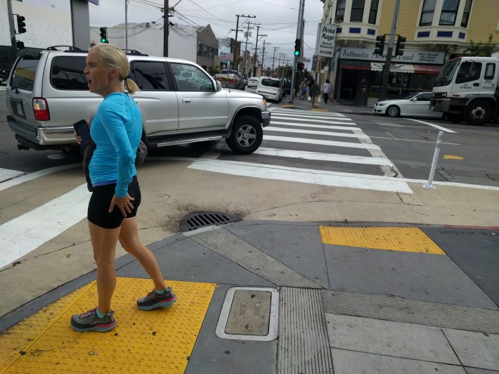 A car turning right sweeping the corner, inviting conflict with cyclists and pedestrians
