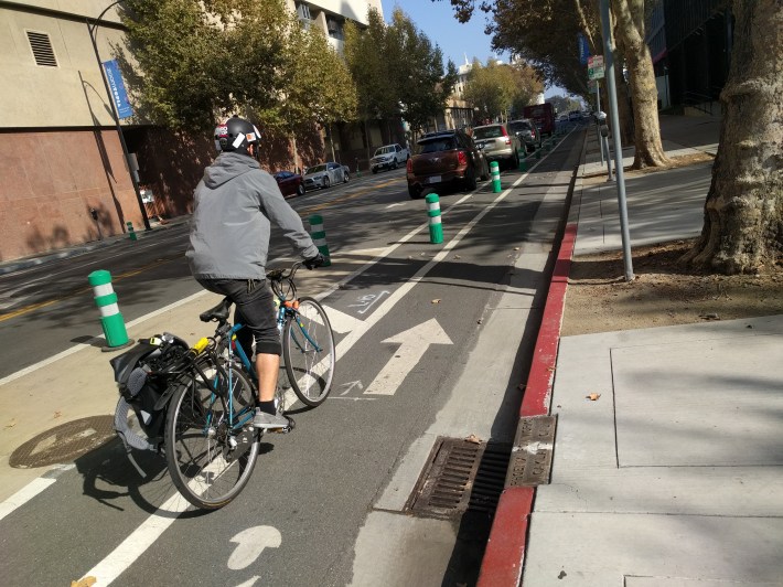 A cyclist navigating one of the new bike lanes. Note the well designed drainage grate with perpendicular slats