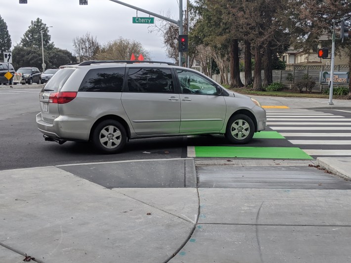 A turning car forced to slow by the curb in the foreground in order to make a turn off Walnut