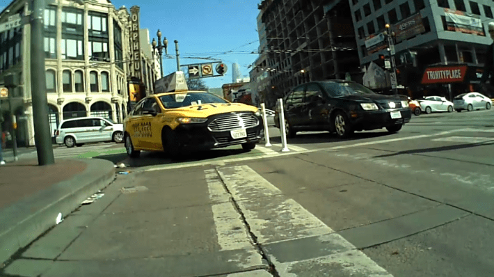 A taxi taking a shortcut through the bike turnout. and a private motorist turning onto Market. Photo: Streetsblog/Rudick -captured from a safety cam, Sat. Feb. 22