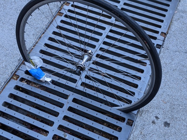 The front wheel of my bike, showing how it fell into one of the gaps between the grates on the ramp in Golden Gate Park (the blue tape is part of a handle I made so it's easier to carry on the bus). Photo: Streetsblog/Rudick